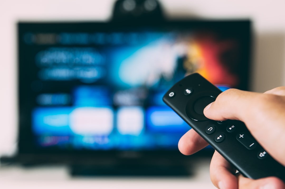 Hand pointing a remote control at a smart TV showing an app interface — refresh rate and picture settings mismatch causing TV flicker.