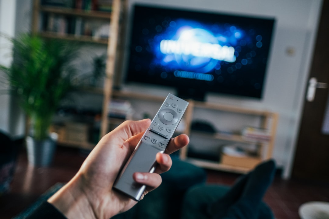 Person holding a Samsung TV remote pointed at a glowing smart television — smart TV screen flickering troubleshooting guide. Photo by Jonas Leupe.