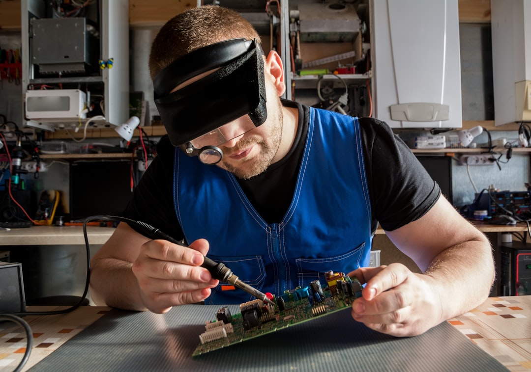 Electronics technician repairing a circuit board under magnifying headset in a repair workshop