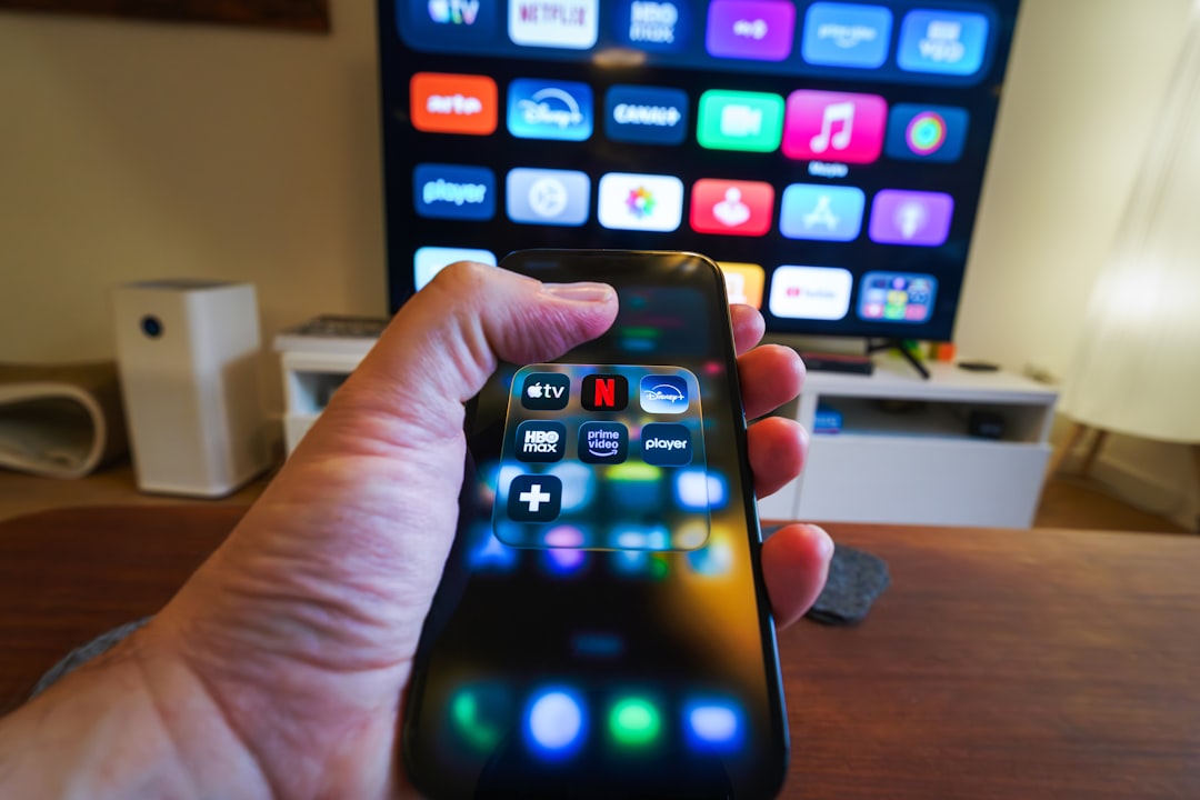 Hand holding a smartphone displaying streaming app icons in front of a smart TV — testing YouTube TV on mobile vs TV
